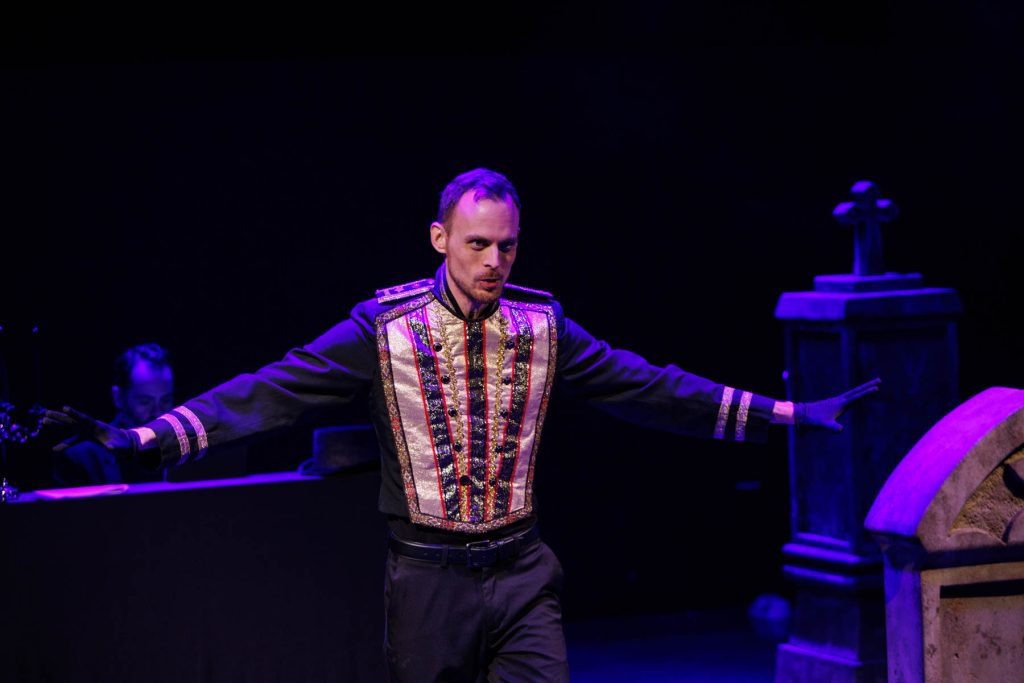 Will Derusha as Mephistopheles sings "Le veau d'or" from Gounod's "Faust," wearing an ornate vest and stretching his arms out menacingly. In the background, Thiago Nascimento accompanies.